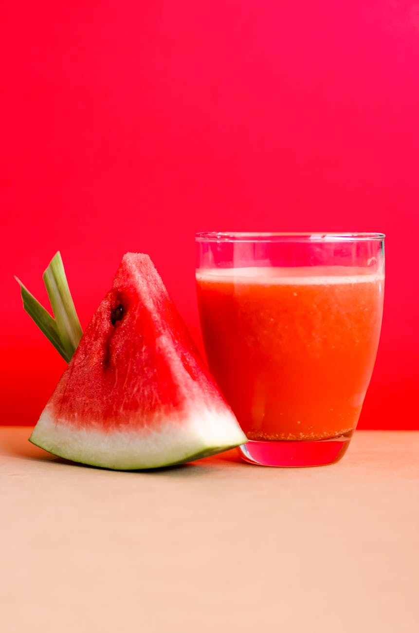 watermelon shake filled glass cup beside sliced watermelon fruit on brown surface